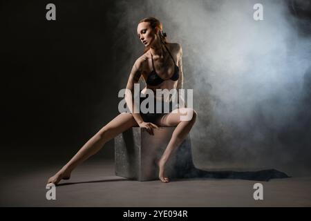 Tänzerin posiert während der Abendvorstellung auf einem Würfel in einem rauchigen Studio Stockfoto