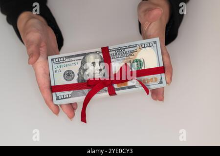 Stapel von 100-Dollar-Banknoten mit Schleife in Frauenhänden zu Designzwecken Stockfoto
