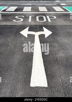 Straßenmarkierungen mit Pfeilen und einem Stoppschild auf dem Boden eines Parkplatzes. Keine Personen. Stockfoto