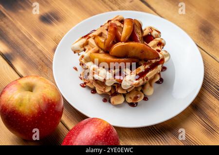 Belgische Waffeln mit Äpfeln in Weinsauce gedünstet auf einem weißen Teller auf hölzernem Hintergrund. Platz für Text. Hochwertige Fotos Stockfoto