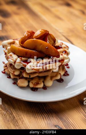 Belgische Waffeln mit Äpfeln in Weinsauce gedünstet auf einem weißen Teller auf hölzernem Hintergrund. Platz für Text. Hochwertige Fotos Stockfoto