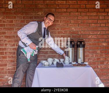 Männlicher Kellner serviert Kaffee und Gebäck in einem ummauerten Garten Stockfoto