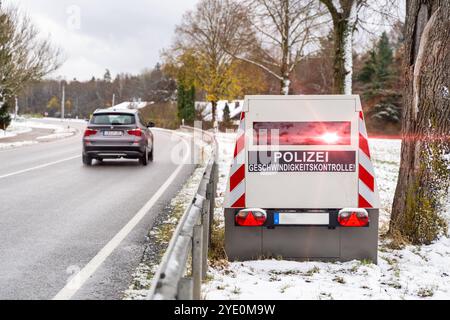 Bayer, Deutschland - 26. Oktober 2024: Ein Radarauflieger der Polizei am Straßenrand mit dem Schild Polizei Geschwindigkeitskontrolle Geschwindigkeitsfalle mit rotem Blinklicht. PHOTOMONTAGE *** ein Blitzeranhänger der Polizei an einem Straßenrand mit Aufschrift Polizei Geschwindigkeitskontrolle Radarfalle mit rotem Blitzlicht. FOTOMONTAGE Stockfoto