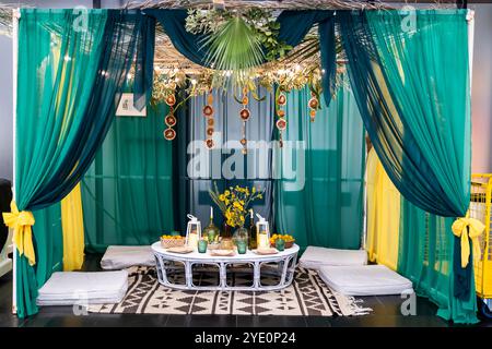 Eine Sukkkah, die für Sukkot gebaut wurde. Eine grün-gelbe Hütte, bedeckt mit Palmblättern, mit einem Tisch im Inneren, der zwei Lampen, Datteln und einen gelben Blumenstrauß enthält Stockfoto