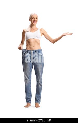 Glückliche schlanke Frau, die eine große Jeans auf weißem Hintergrund anprobiert Stockfoto