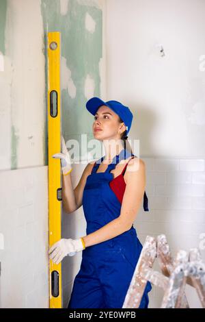 Attraktive junge Bauherrin in Arbeitskleidung gekleidet, die den Füllstand im Renovierungsprozess überprüft Stockfoto