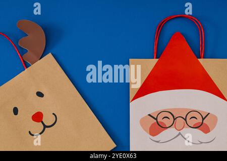 Weihnachtskomposition mit Weihnachtsgeschenktaschen mit Weihnachtsmann und braunem Rentier auf blauem Hintergrund. Minimales Weihnachts- und Neujahrskonzept. Stockfoto