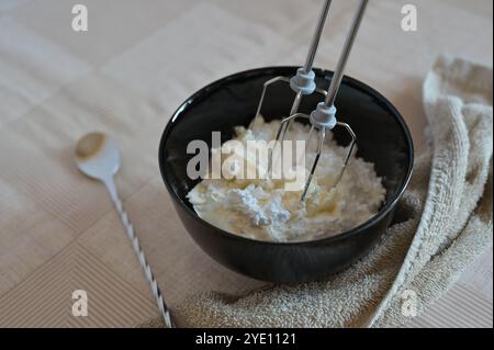 Zubereitung und Schlagen der Sahne mit einem Mixer für Brötchen in einer schwarzen Schüssel Stockfoto