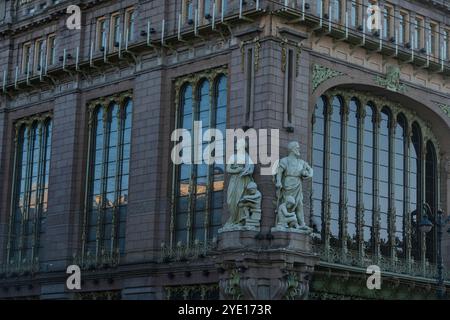 Detaillierter Blick auf eine historische Gebäudefassade mit Statuen und großen Bogenfenstern mit komplizierten Designelementen. Das Bild hebt die Architektur hervor Stockfoto