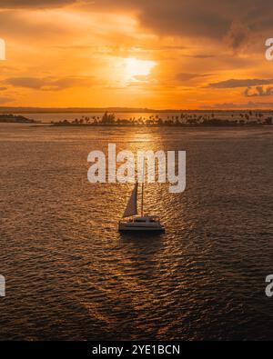 Ein Segelboot gleitet während Eines lebendigen Sonnenuntergangs über Ein ruhiges Meer mit goldenen Reflektionen auf dem Wasser und dramatischen Wolken im Himmel in der Nähe von Old San Juan, Pu Stockfoto