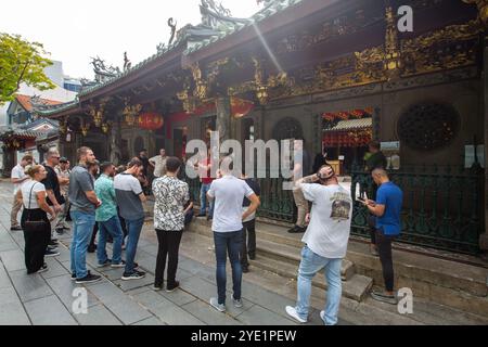 Eine Gruppe von USA-Touristen steht vor dem Eingang des Thian Hock Keng Tempels und hört dem Reiseleiter, der über Geschichte und architektonische Details in Singapur spricht. Stockfoto