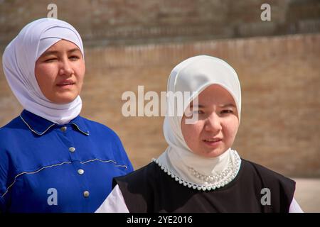 Buchara, Usbekistan; 19. September 2024: Zwei junge usbekische Frauen mit eleganten weißen Schleiern vor der malerischen Kulisse von Buchara, Usbekista Stockfoto