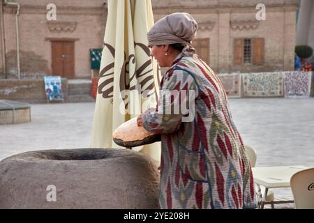 Chiwa, Usbekistan; 21. September 2024: Eine usbekische Frau, die traditionelles Brot auf dem historischen Hauptplatz von Chiwa, Usbekistan, backt. Ich trage einen farbenfrohen Patt Stockfoto