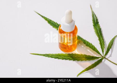 Tropfflasche gefüllt mit Cannabisöl auf einem Hintergrund mit Marihuanablättern auf weißem Hintergrund, medizinisches Cannabis Stockfoto
