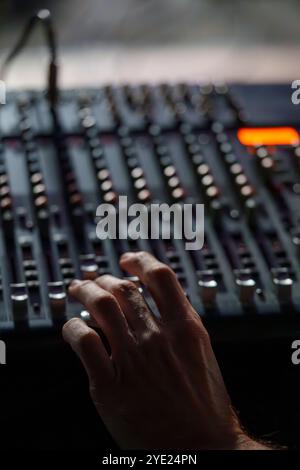 Nahaufnahme einer Hand, die eine Audio-Mischkonsole in einem schwach beleuchteten Studio, Professional Sound Engineering Setup, bedient Stockfoto