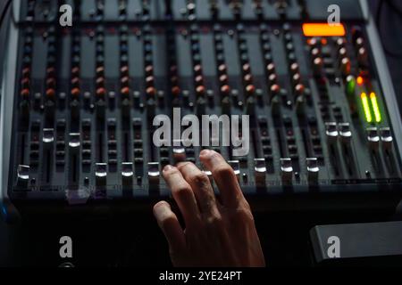 Nahaufnahme einer Hand, die eine Audio-Mischkonsole in einem schwach beleuchteten Studio, Professional Sound Engineering Setup, bedient Stockfoto