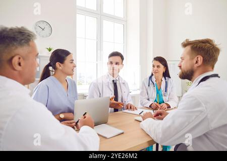 Selbstbewusstes Arzttreffen, Chirurgen, Schwesternpersonal in weißer medizinischer Uniform mit Kollegen am Schreibtisch Stockfoto