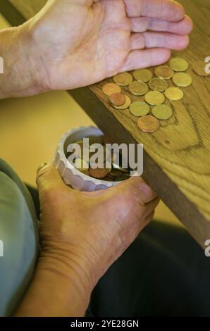 Seniorhände für Erwachsene sortieren kleine Wechselgeld in einen Behälter auf einem Holztisch. Hochwertige Fotos Stockfoto