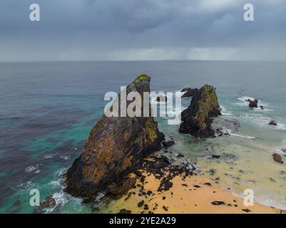 Aus der Vogelperspektive gezackte Felsformationen vor einem Küstenstrand mit Regen bei Narooma an der Südküste von New South Wales, Australien. Stockfoto