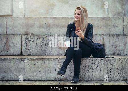 Telefon, Kaffee und Frau auf Treppen in der Stadt am Morgen für die Buchung der Unterkunft über die mobile App. Urlaubs-, Touristen- und weibliche Person mit Cappuccino und Stockfoto