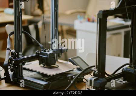 Nahaufnahme zweier fortschrittlicher 3D-Drucker in einem modernen Arbeitsbereich, wobei ein Element gedruckt wird. Geräte und Werkzeuge sind um die Maschinen herum sichtbar, was die Produktivität unterstreicht Stockfoto