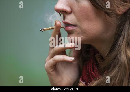 Closeup 3/4-Schuss aus der unteren Hälfte des Gesichts der kaukasischen Frau rauchend Hand gerollte Marihuana-Gelenke. Cannabiszigarette im Freien von einer nervösen Frau geraucht Stockfoto