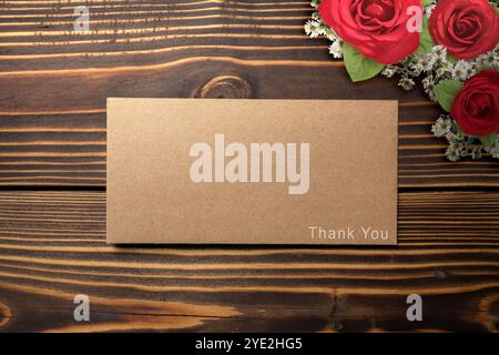 Blick von oben auf braunen Umschlag und Postkarte mit Rosenblumen und Worten Danke, dass Sie auf hölzernem Hintergrund darauf geschrieben haben. Vielen Dank für die Präsentation o Stockfoto