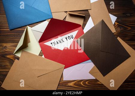 Draufsicht des roten Umschlags und der Postkarte mit weißer Karte mit Wörtern Danke, dass Sie darauf auf einem Stapel Umschlag und einer Postkarte auf hölzernem Hintergrund geschrieben haben. Danke Stockfoto