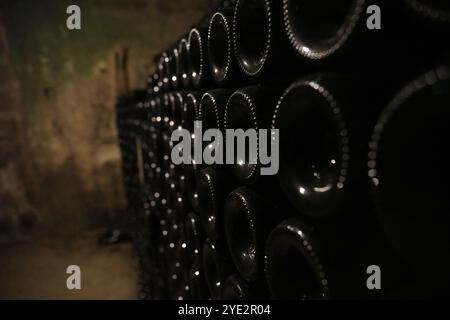 Nahaufnahme von vielen Flaschen Rotwein, die kopfüber in einem alten hölzernen quadratischen Gebäude in einer alten Kellerhöhle aus Tuff gestapelt sind. Stockfoto