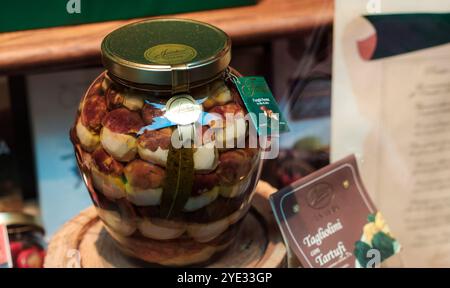 Ein großer Glasbehälter gefüllt mit verschiedenen Trüffeln wird auf einem Markt in Alba, Italien, ausgestellt. Die lebhaften Farben und Texturen laden zum Laden ein Stockfoto