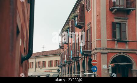 In Alba, Italien, bieten elegante Gebäude farbenfrohe Fassaden und unverwechselbare Architektur. Balkone mit Pflanzen überblicken eine belebte Straße, cr Stockfoto