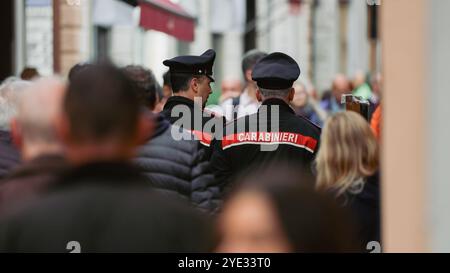 Zwei Polizisten in Uniform laufen durch eine geschäftige Straße in Alba, Italien, während die Menschen an einem lebhaften Nachmittag vorbeikommen Stockfoto