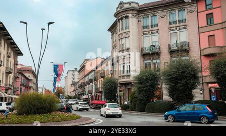 Eine lebhafte Straße in Alba Italien zeigt elegante historische Gebäude, eingebettet in moderne Fahrzeuge. Der bewölkte Himmel wirft ein sanftes Licht auf das pulsierende Stadtl Stockfoto