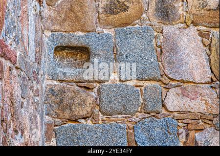 Avila, Spanien - 11. Februar 2023: Ein rechteckiges, geschnitztes Loch in einem Steinblock, der Teil einer mittelalterlichen Gebäudemauer ist. Stockfoto
