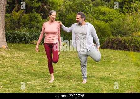 Reife Paare genießen gemeinsam Outdoor-Übungen und balancieren auf einem Bein im Park Stockfoto