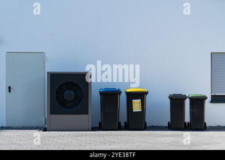 Neben vier farbenfrohen Recyclingbehältern steht eine Sammelanlage für Großmüll vor einer einfachen Wand, die die organisierte Abfallwirtschaft in einer städtischen Umgebung veranschaulicht. Stockfoto