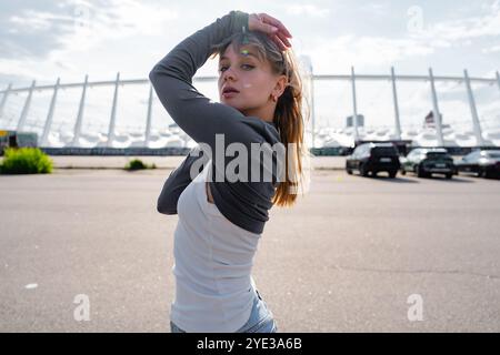 Junge Frau posiert selbstbewusst draußen in der Nähe eines Sportstadions an einem sonnigen Tag Stockfoto