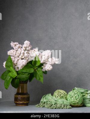 Bouquet von üppigen weißen Fliedern in dunkler Vase auf grauem Hintergrund. Kleine weiße Blüten stehen im Kontrast zu grünen Blättern und heben sich auf einer dunklen Vase hervor, die still ist Stockfoto