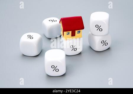 Ein kleines Haus, umgeben von Würfeln mit Prozentzeichen. Grundsteuer, Grundstückskostenkonzept. Stockfoto