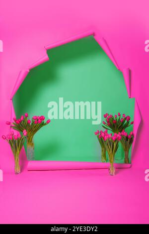 Ein heller Frühlingshintergrund aus rosa zerrissenem Papier und eine grüne Wand mit Tulpen. Die Fotozone der Blume. Eine Kombination aus Rosa und Grün. Stockfoto