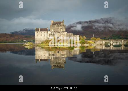 Das Sonnenlicht beleuchtet Eilean Donan Castle, das sich im Loch Duich mit Scotch-Nebel im Hang hinter den Highlands, Schottland, spiegelt Stockfoto