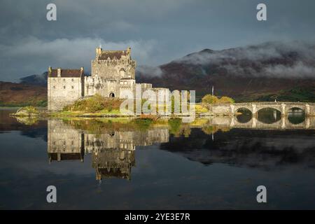 Das Sonnenlicht beleuchtet Eilean Donan Castle, das sich im Loch Duich mit Scotch-Nebel im Hang hinter den Highlands, Schottland, spiegelt Stockfoto