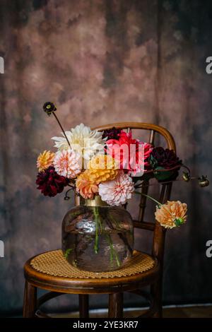 Großer Strauß aus Herbstblumen Dahlien und Astern in Orange-, Burgunderrot-, weiß- und Gelbtönen in einer Vase, die auf einem Vintage-Bugholzstuhl steht Stockfoto