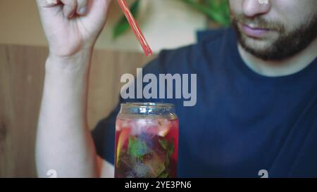 Blumen in Vasen im Hintergrund schaffen eine ruhige Atmosphäre für diesen erfrischenden Moment. Der junge Mann spürt den Sommer, wenn er einen kühlen Cocktail schlürft Stockfoto