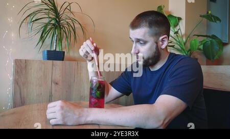 Bei einem kühlen Cocktail spürt der junge Mann die Sommeratmosphäre. Blumen in Vasen im Hintergrund schaffen eine ruhige Atmosphäre für diese Erfrischung Stockfoto