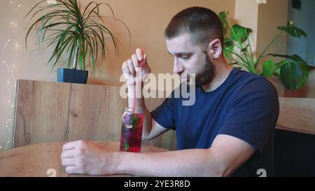 Bei einem kühlen Cocktail spürt der junge Mann die Sommeratmosphäre. Blumen in Vasen im Hintergrund schaffen eine ruhige Atmosphäre für diese Erfrischung Stockfoto