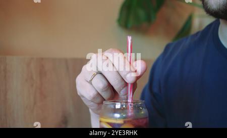 Bei einem kühlen Cocktail spürt der junge Mann die Sommeratmosphäre. Blumen in Vasen im Hintergrund schaffen eine ruhige Atmosphäre für diese Erfrischung Stockfoto