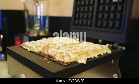 Der Prozess der Herstellung herzhafter Waffeln wird zum Leben erweckt, wenn eine junge Frau den Teig zubereitet und in einen elektrischen Waffelautomaten gießt. Achtung Stockfoto