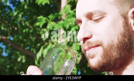 Er schlürft einen coolen Cocktail und macht eine Pause im Freien. Umgeben von lebhaftem Sommerlaub, genießt er den erfrischenden Geschmack des Sommers. Stockfoto