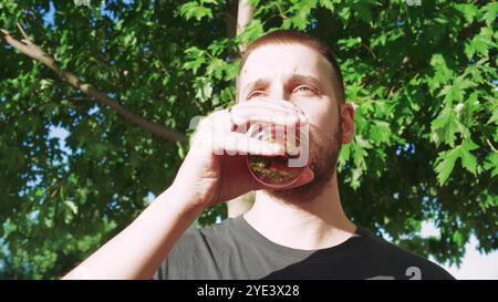 Er schlürft einen coolen Cocktail und macht eine Pause im Freien. Umgeben von lebhaftem Sommerlaub, genießt er den erfrischenden Geschmack des Sommers. Stockfoto